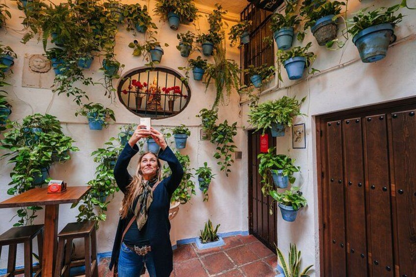 Una persona tomándose un selfie en un patio rodeado de macetas con plantas y una puerta de madera. 4