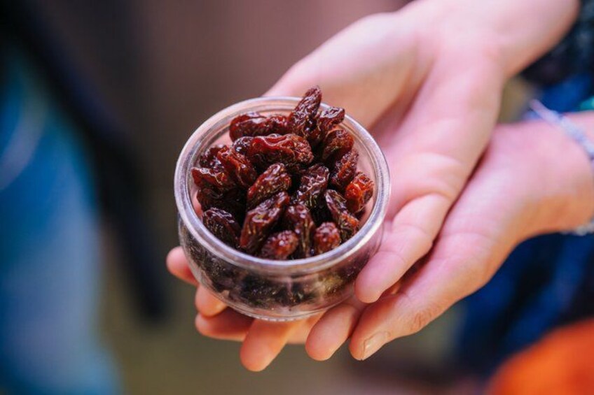 A person holding a small glass jar filled with dried red berries. 5