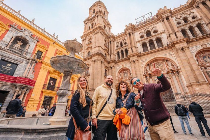 A historic building with ornate architecture, a fountain, and people posing for a photo. 3