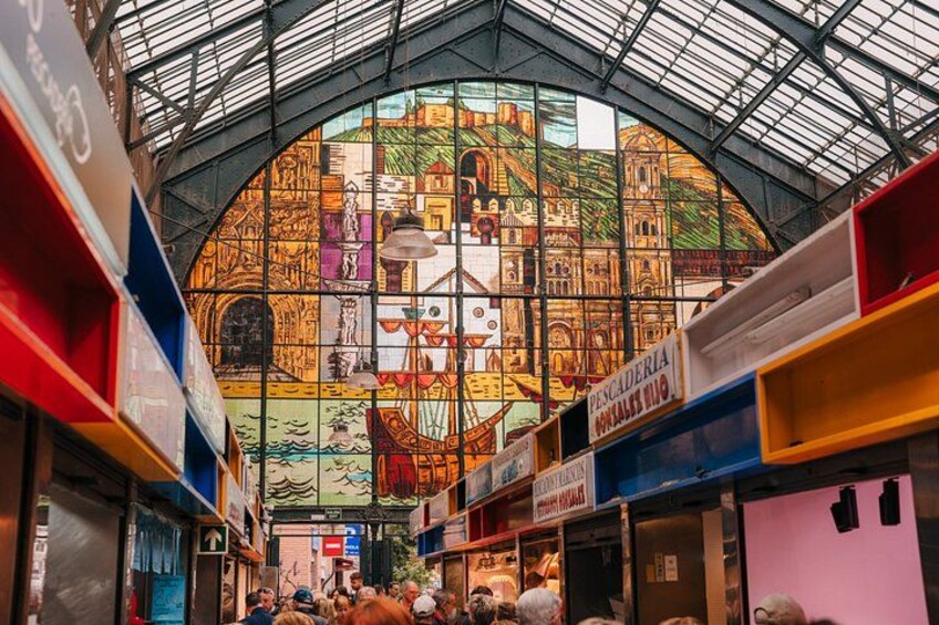A vibrant indoor market with colorful stalls and a large stained glass window in the background. 4