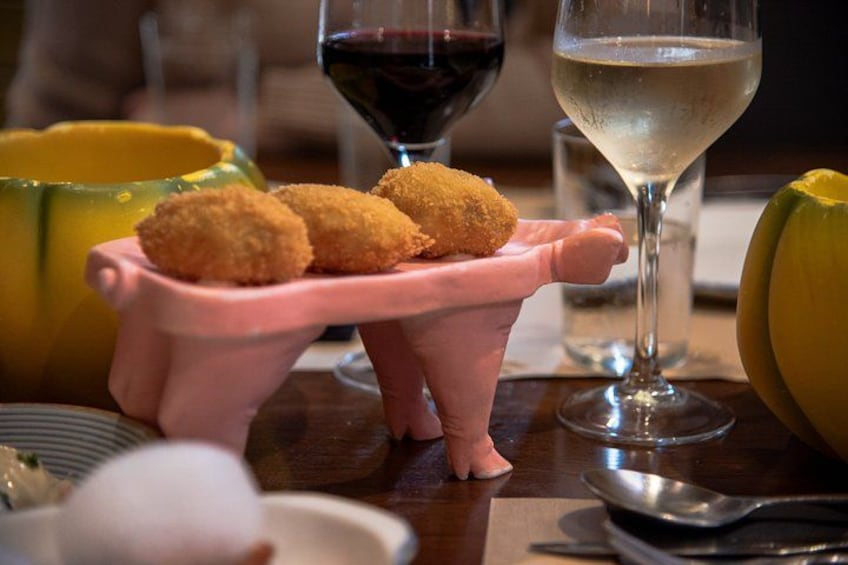 A pink serving tray with croquettes, a glass of red wine, and a glass of white wine on a table. 2