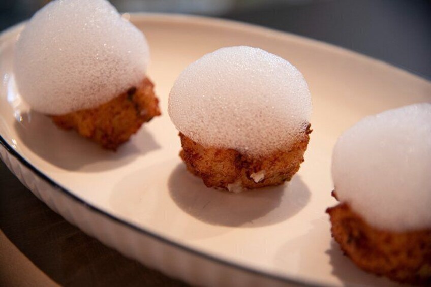 Three fried food items topped with white foam on a plate. 4