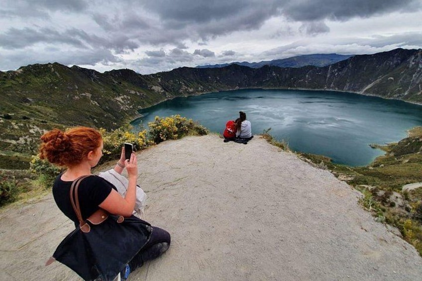 A woman taking a photo of a lake surrounded by mountains. 2