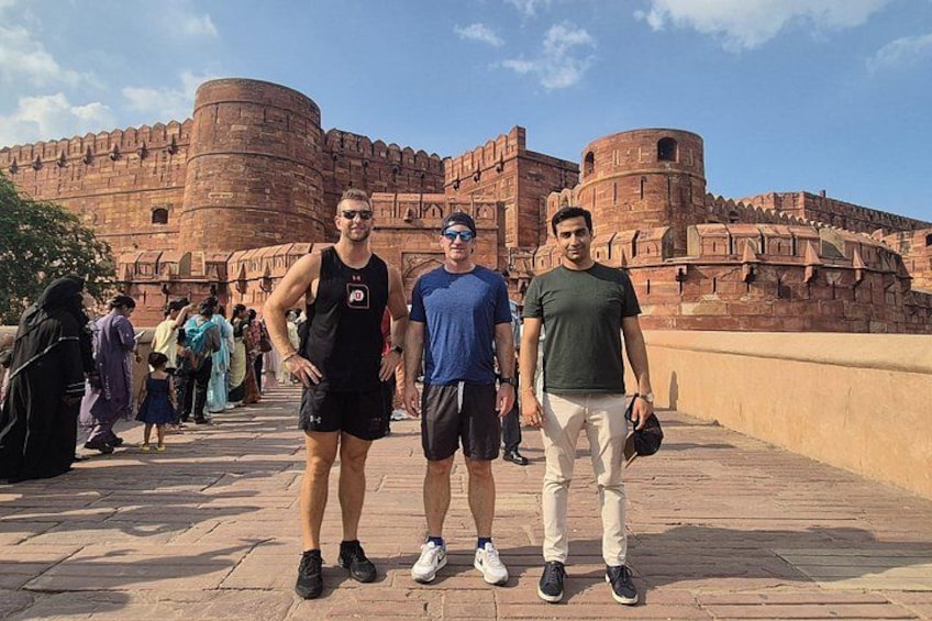 Tres hombres de pie frente a una gran fortaleza histórica bajo un cielo despejado. 2