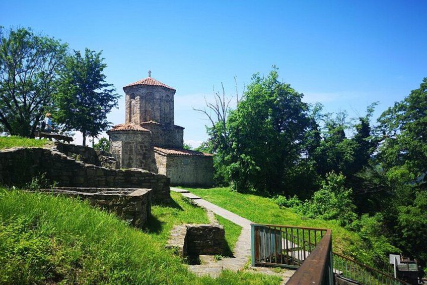 A historical stone structure with a tower, surrounded by lush greenery and a clear sky. 3