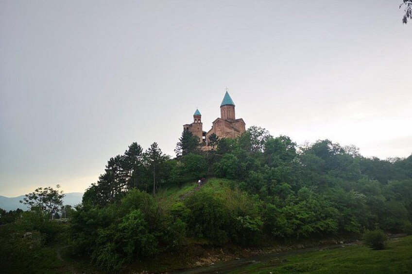 A historic building with two towers on a hill, surrounded by dense greenery. 5