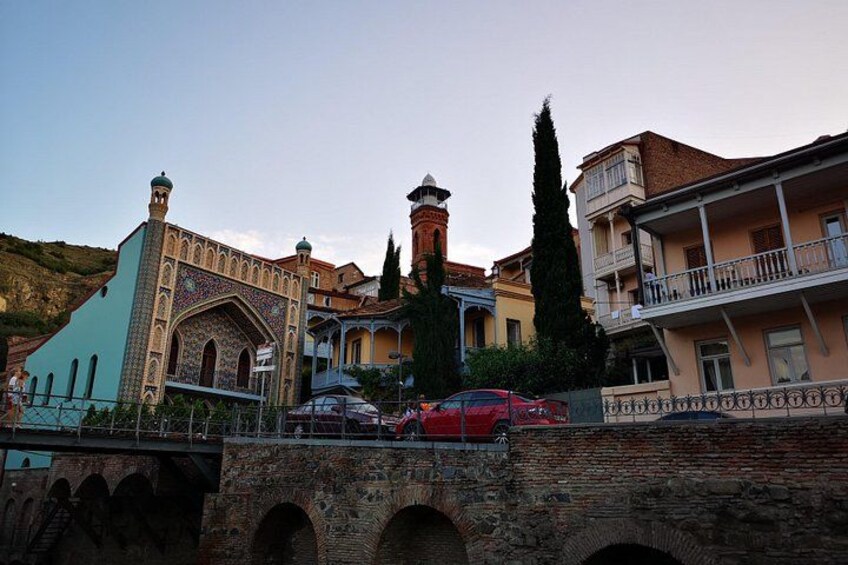 A historic bridge with arches, a mosque with intricate tile work, and residential buildings with balconies. 1