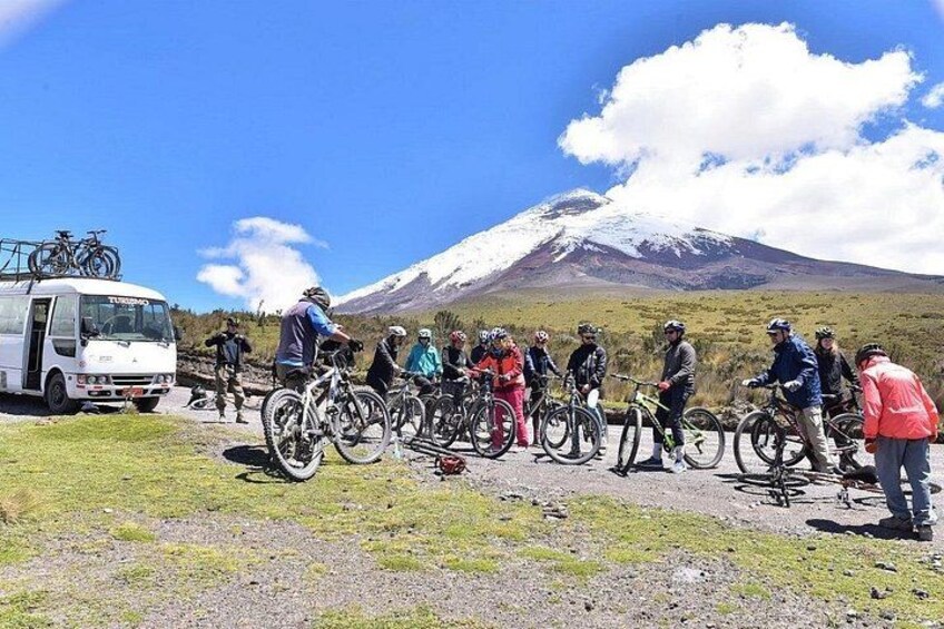 A group of cyclists gathered around a vehicle, with a mountain and a clear sky in the background. 2