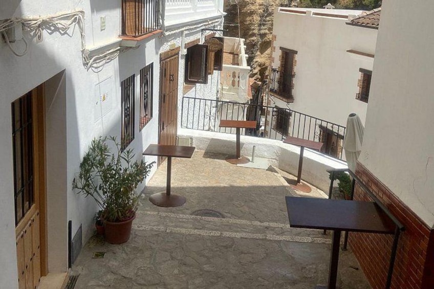 A narrow courtyard with a potted plant, a table, and a bench. 2