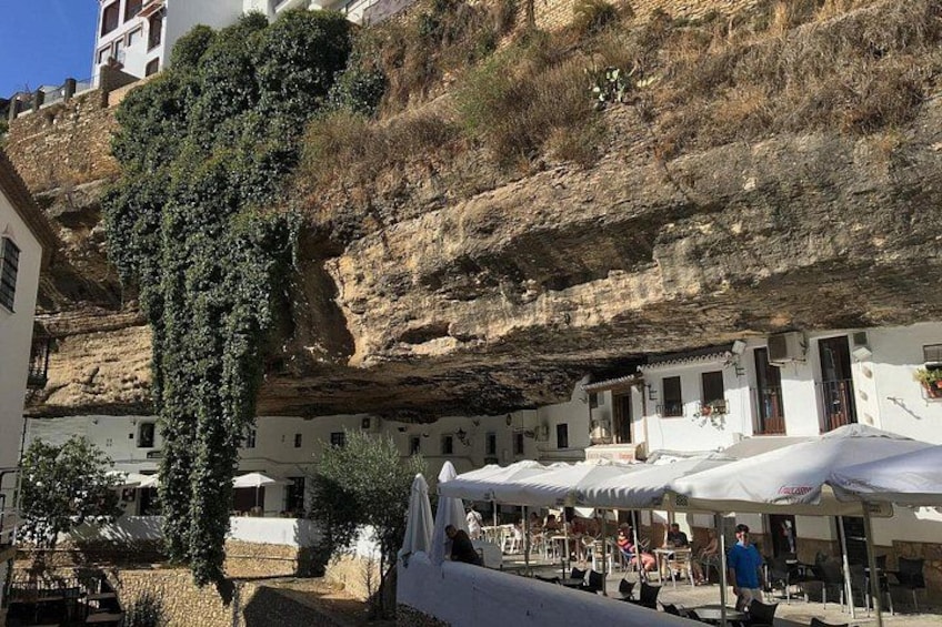 A cliffside with buildings, a tree, and outdoor seating. 4