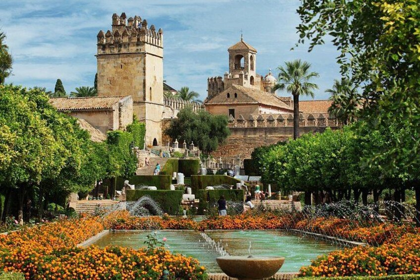 A historic castle with a tower, surrounded by a garden with orange flowers and a fountain. 1