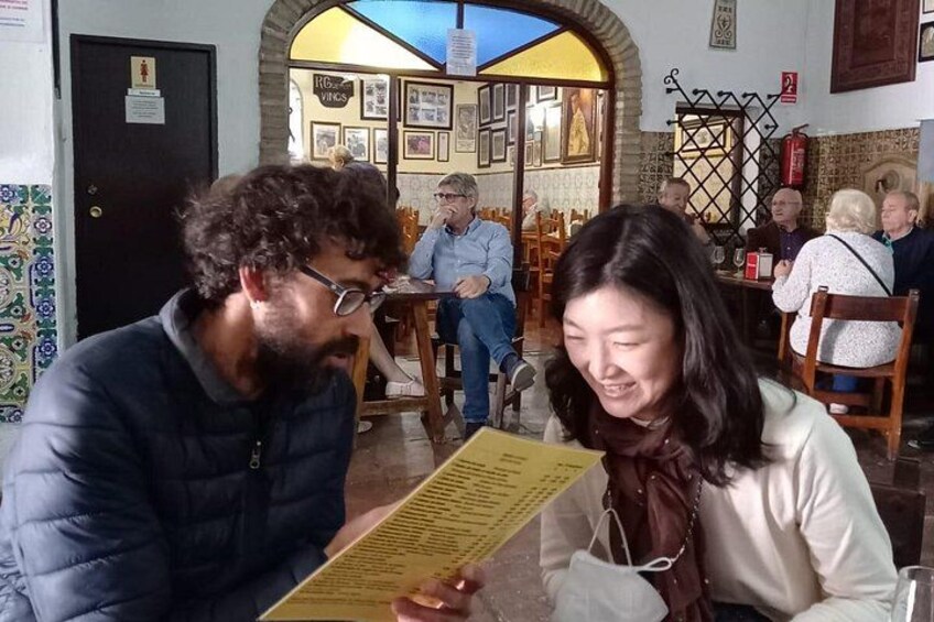 A restaurant interior with patrons seated at tables, a menu, and a tiled wall. 5