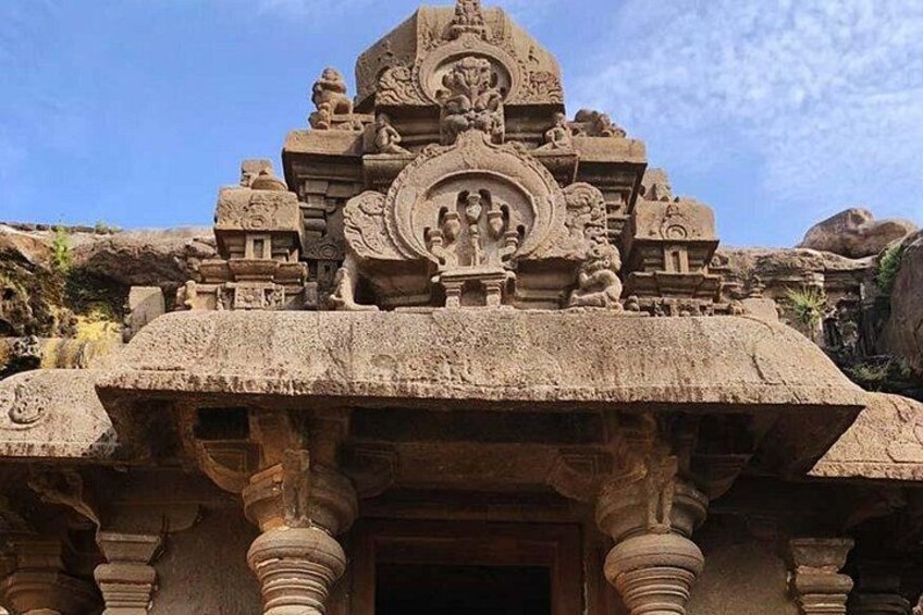A stone temple with intricate carvings, a central deity figure, and a surrounding structure. 3