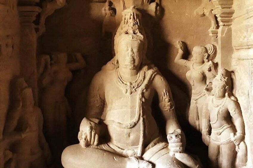 A stone sculpture of a seated figure with a large head and multiple arms, surrounded by smaller figures. 2