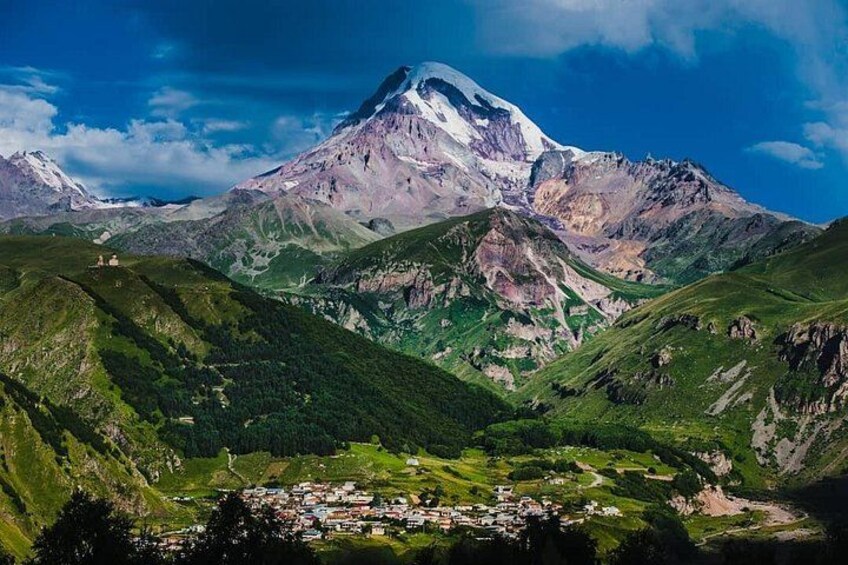 Een berg met een besneeuwde top, een groene vallei en een kleine nederzetting aan de voet ervan. 2