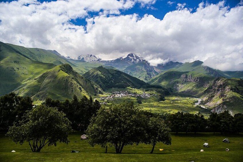 Un paisaje montañoso con un valle, árboles y un pequeño asentamiento. 2