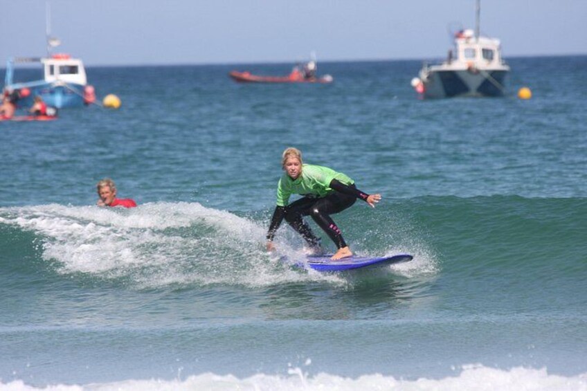 A person surfing on a wave with a blue surfboard, another person in the water, and boats in the background. 5