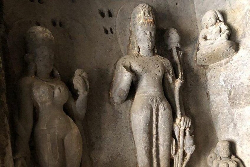 A stone sculpture of a standing figure holding a staff and a small object, with a smaller figure beside it. 2
