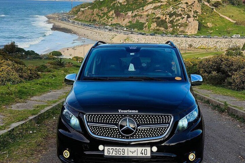 A black Mercedes-Benz Tourismo parked on a coastal road with a view of the ocean and hills. 2