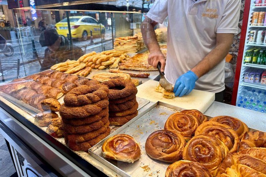 Eine Bäckertheke mit verschiedenen Backwaren und einer Person, die ein Gebäckstück anschneidet. 1