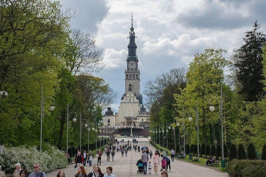 A large tower with a spire, surrounded by trees and a crowd of people walking on a wide path. 2