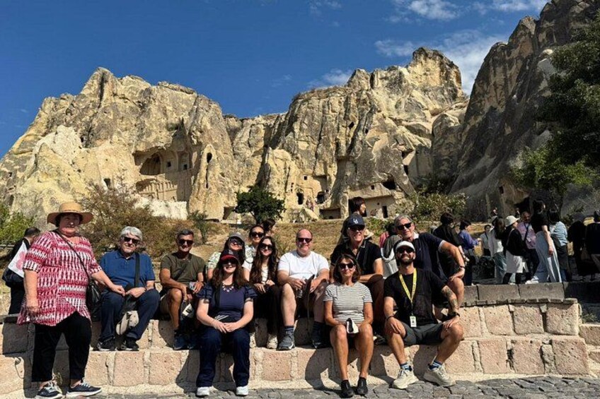A group of people sitting on a stone ledge with a rocky mountain backdrop. 2