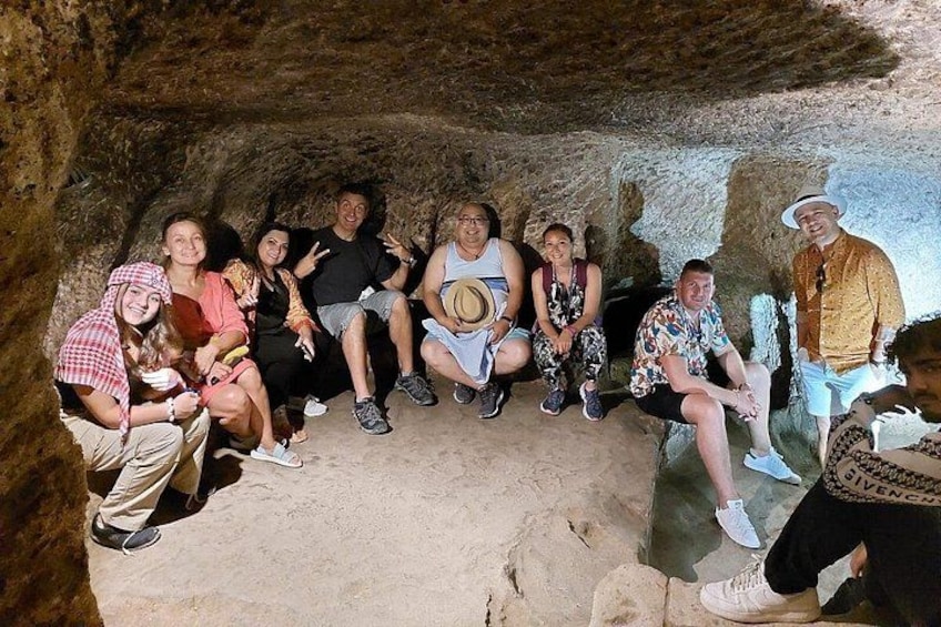 A group of people sitting in a cave with rocky walls and a sandy floor. 5