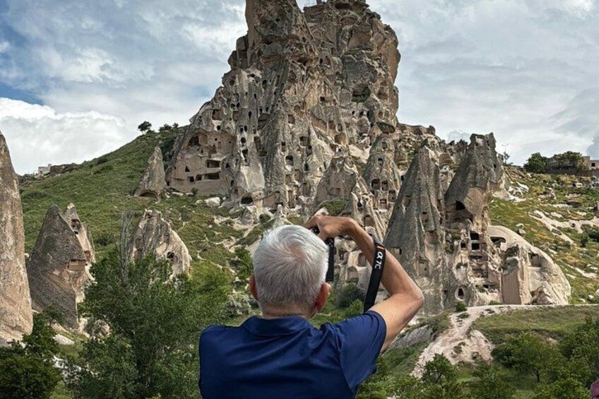 A man taking a photo of a rocky landscape with numerous cave dwellings. 3