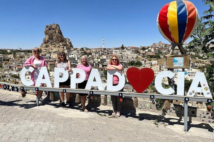 A sign with the words 'Cappadocia' and a heart symbol, with a hot air balloon in the background. 1