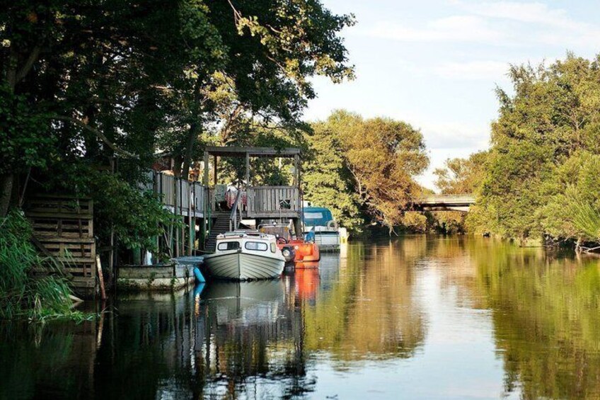Une rivière paisible où des bateaux sont amarrés à un quai en bois, le tout entouré d’une végétation luxuriante. 2