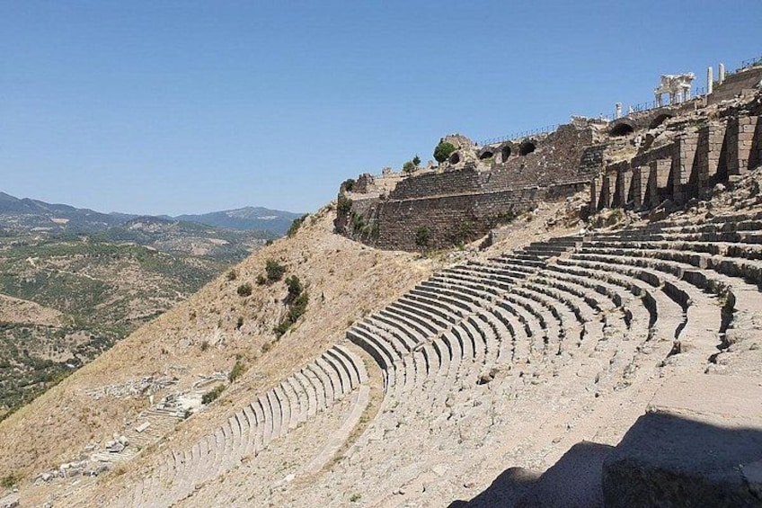 An ancient amphitheater with tiered seating and ruins on a hillside. 2
