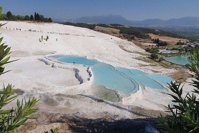 Terraced pools of turquoise water, white travertine formations, and a distant mountain range. 3