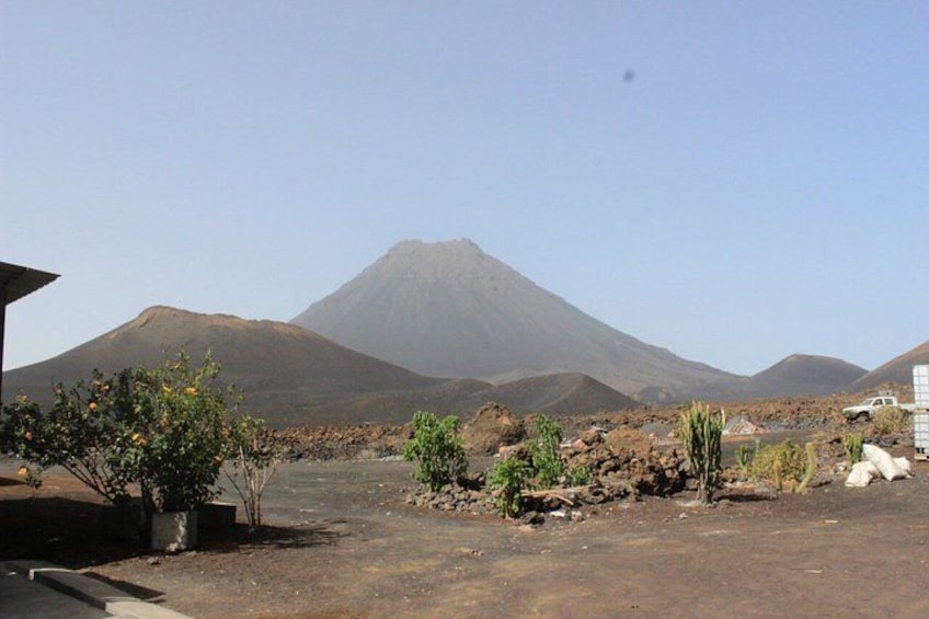 A volcanic landscape with a prominent mountain in the background, a paved road, and sparse vegetation. 3
