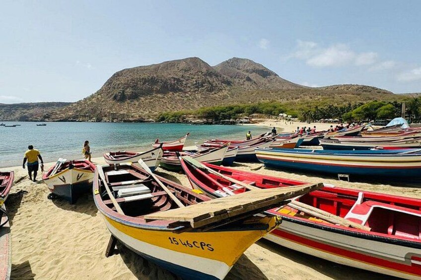 A beach with several colorful boats docked, a sandy shore, and a mountain in the background. 5