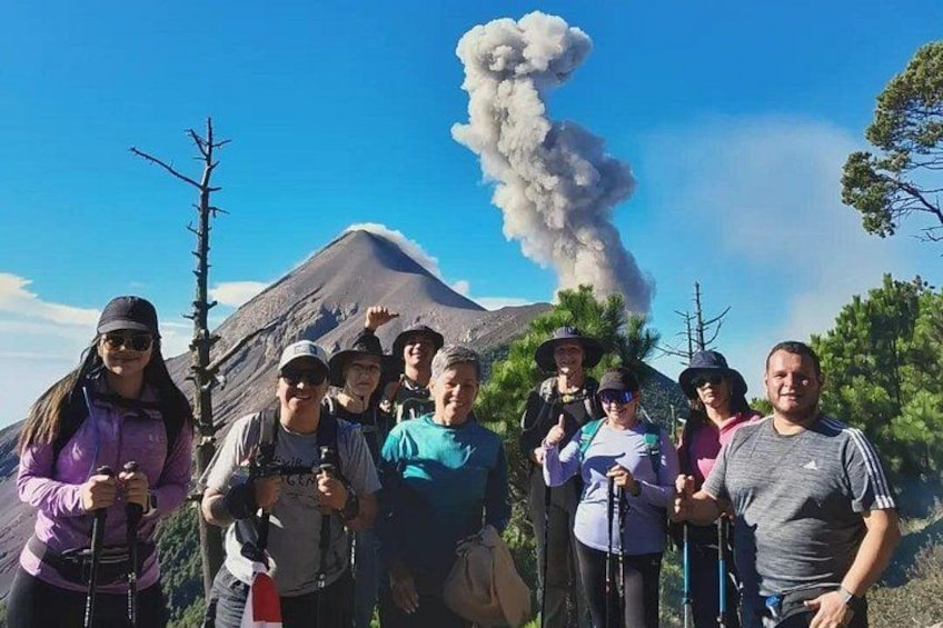 A group of people with hiking gear in front of a mountain with a smoke plume. 4