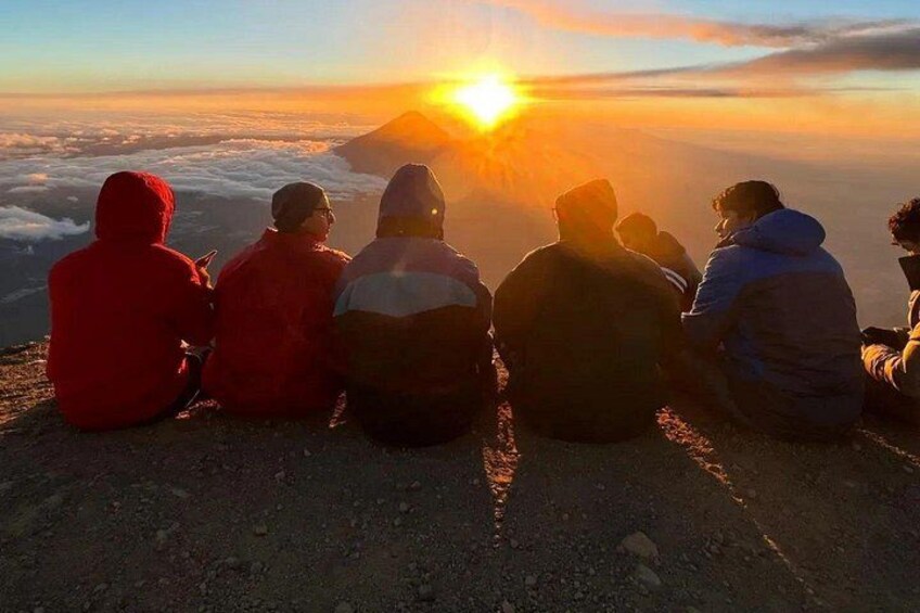 A group of people sitting on a mountain ridge during sunset. 3