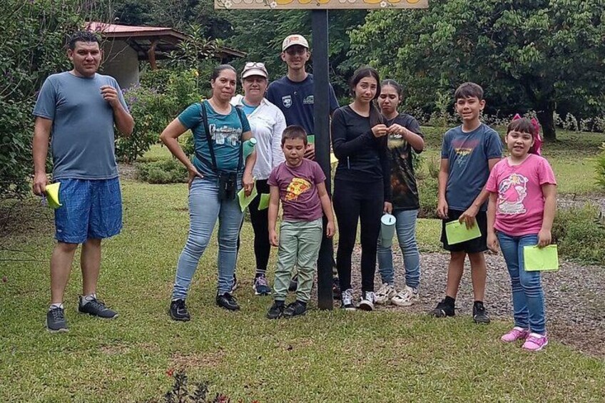A group of people standing outdoors, some holding green objects, with a grassy area and trees in the background. 5