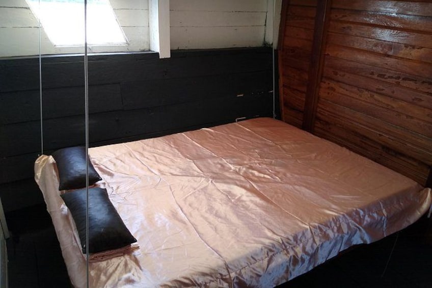 A small, dimly lit room with a single bed covered in a light-colored sheet. 3