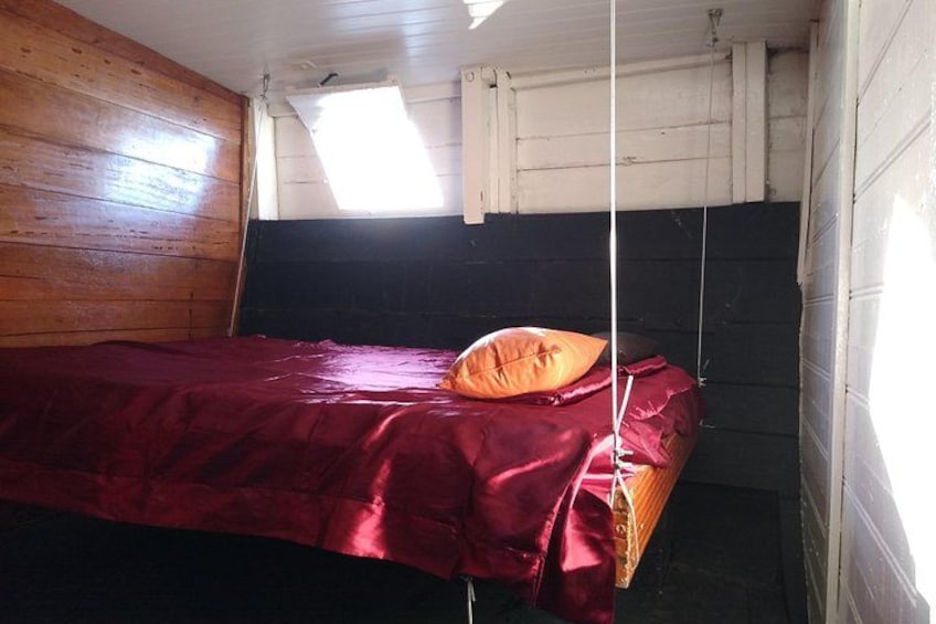 A small, dimly lit room with a single bed, a window, and wooden walls. 5