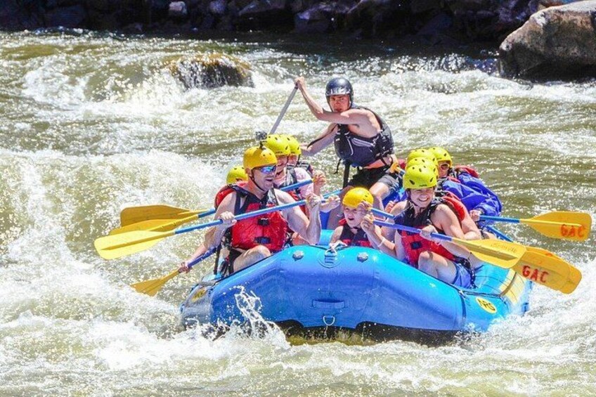 A group of people in a blue raft navigating a river with rapids. 3