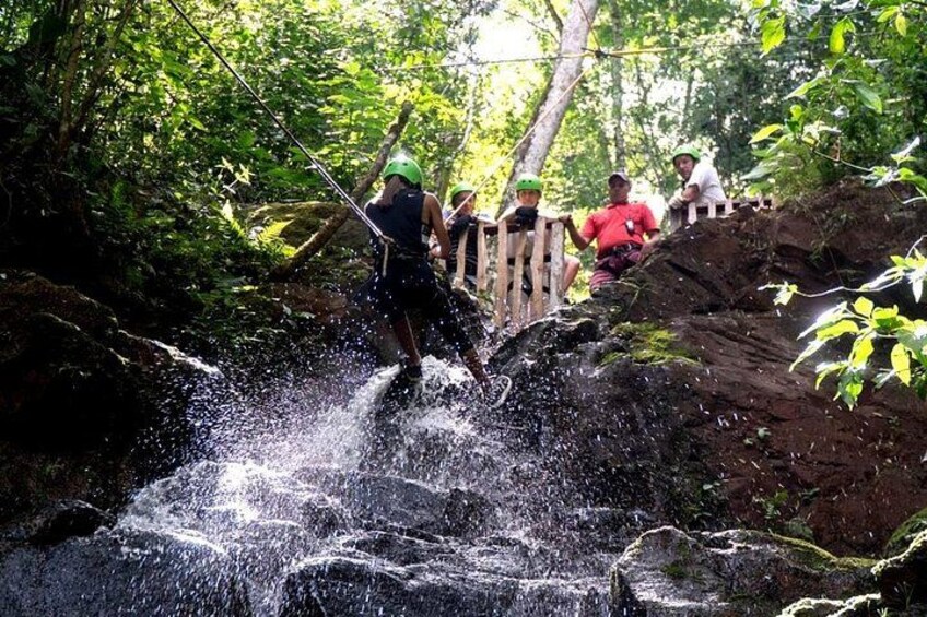 A person jumping over a waterfall in a forested area. 3