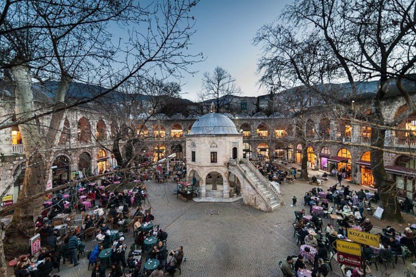 A courtyard with people sitting at tables, surrounded by arches and a central dome structure. 5