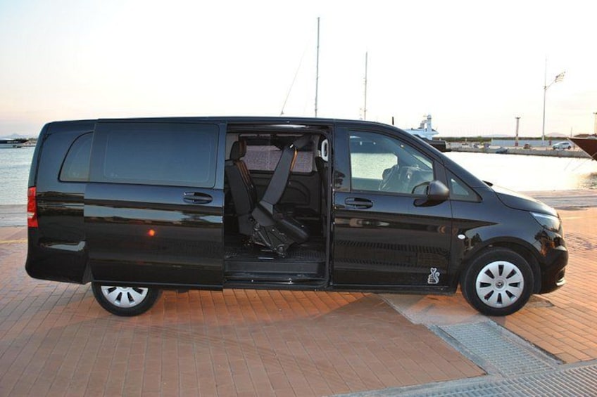 A black van parked on a brick surface near a body of water with a sailboat in the background. 3