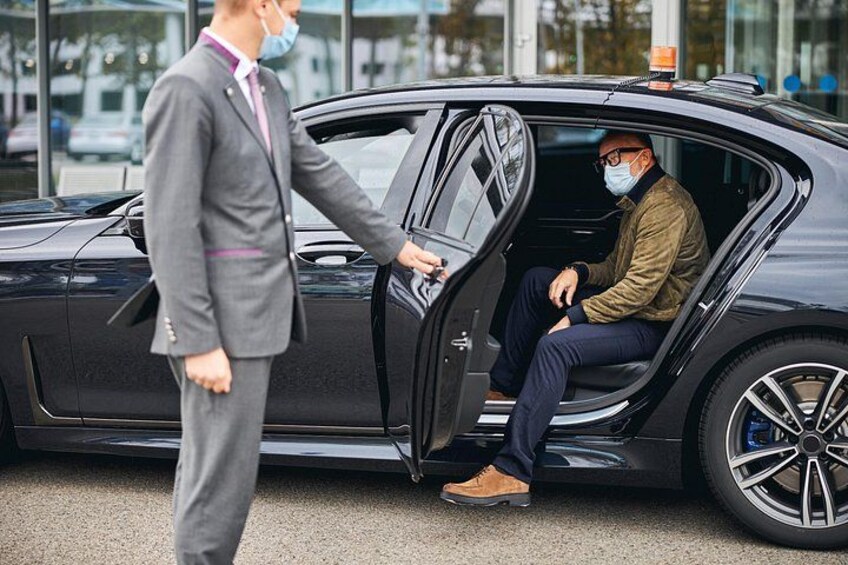 A man in a suit standing next to a car with a man sitting inside. 2