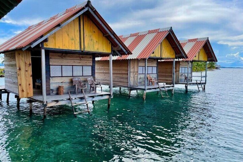 Overwater bungalows with wooden structures and metal roofs, surrounded by clear turquoise water. 4