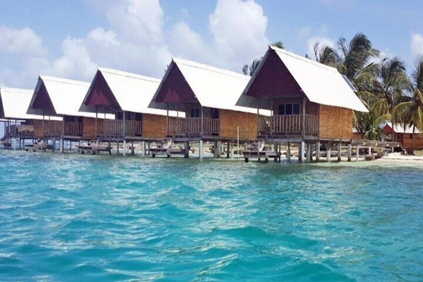 Overwater bungalows with wooden structures and white roofs, surrounded by turquoise water and palm trees. 5