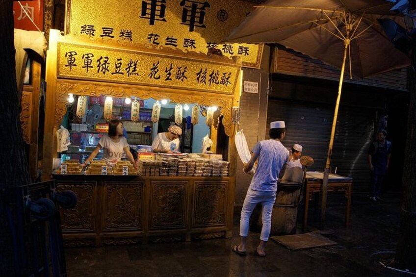 A street food stall with a sign in a foreign language, a person serving food, and another person carrying a tray. 2