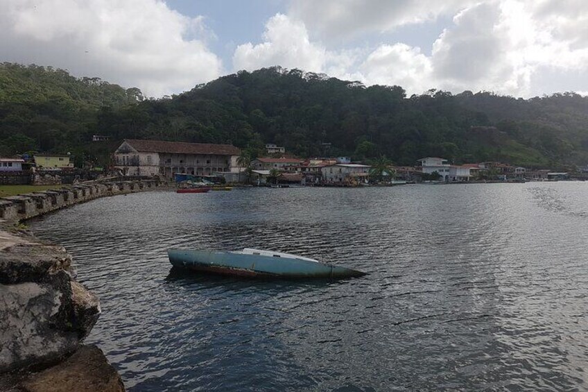A calm harbor with a small boat anchored near the shore, surrounded by buildings and lush greenery. 5