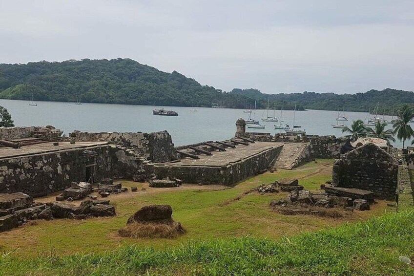 Ancient ruins by a calm lake with boats and a ship in the distance. 4