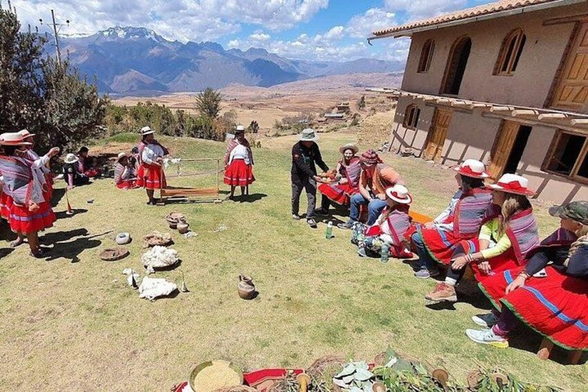 Un gruppo di persone in abiti tradizionali riunite all'aperto, alcune in piedi e altre sedute, con un paesaggio montuoso sullo sfondo. 3